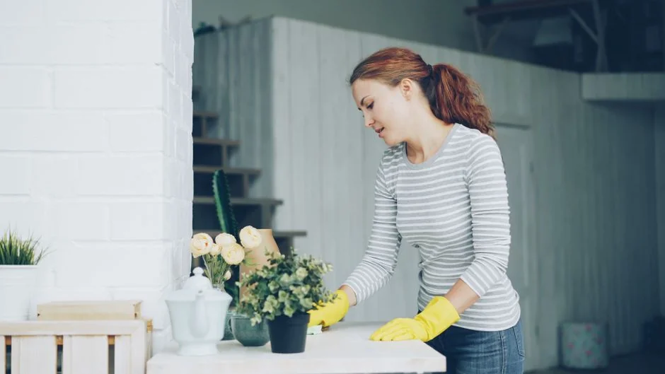 A woman carefully wraps a sofa in protective material while packing boxes in a bright room.